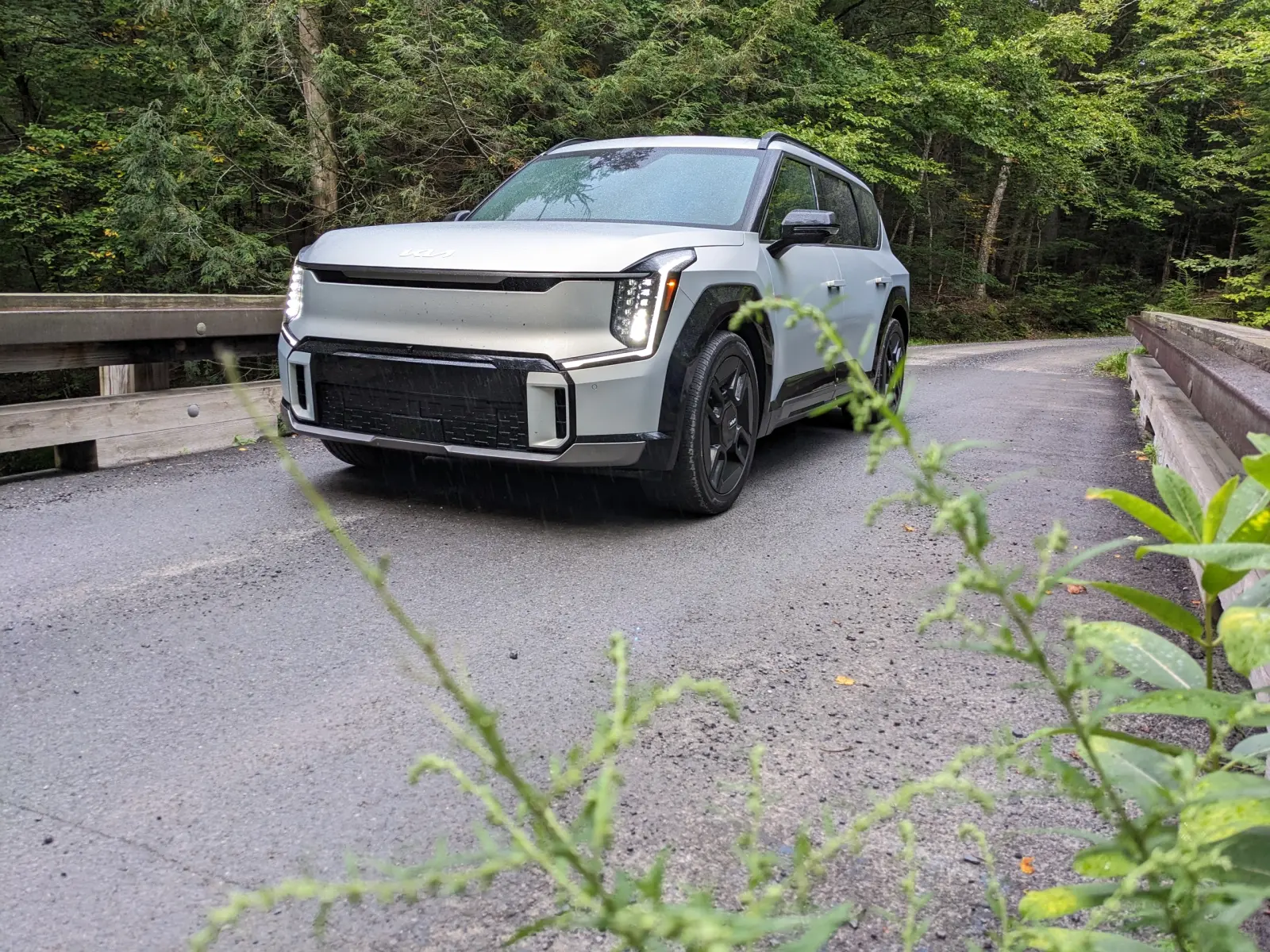 The Kia EV9 crossing a one-lane timber bridge on a wet gravel forest road