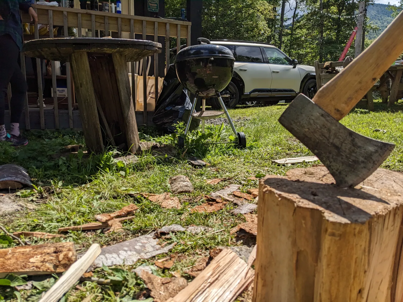 An axe in a chopping block with split firewood and the Kia EV9 parked in the background